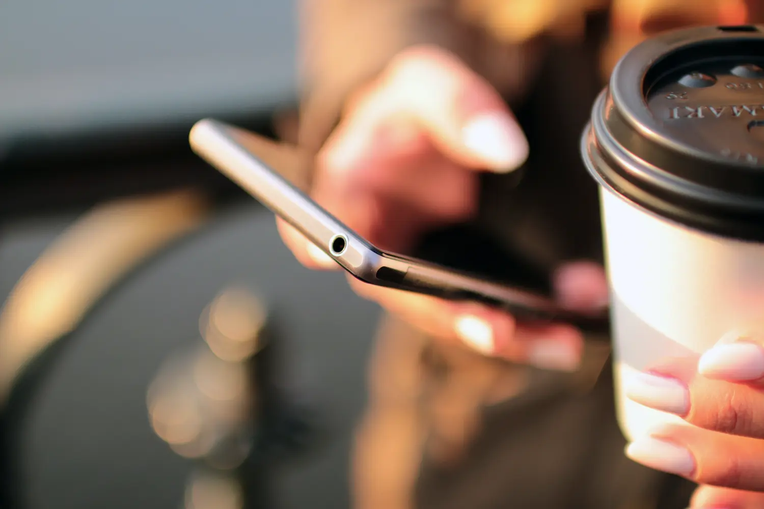 Eine Person, die in der einen Hand eine Kaffeetasse und in der anderen ein Handy hält